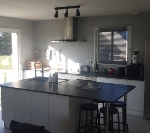 Cuisine ouverte avec îlot central noir et tabourets de bar – réalisation L'atelier du Sahuc